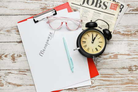 Clipboard with word MENOPAUSE, eyeglasses, newspaper and alarm clock on light wooden backgroundの写真素材