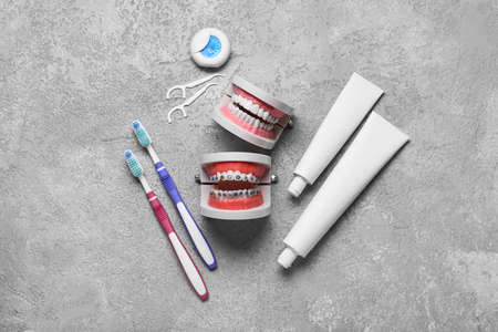 Model of jaws with braces, dental floss, toothbrushes and paste on gray background