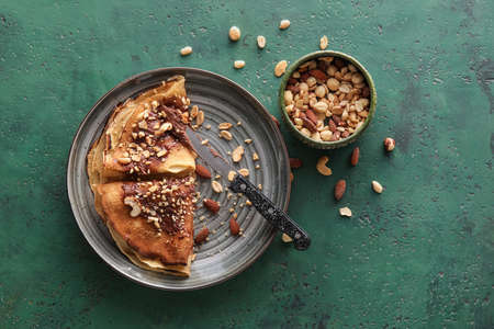 Plate of tasty thin pancakes with chocolate paste and nuts on green backgroundの写真素材
