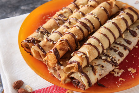 Plate of tasty thin pancakes with chocolate paste and nuts on table, closeup