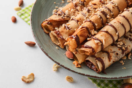 Plate of tasty thin pancakes with chocolate paste and nuts on white background, closeup