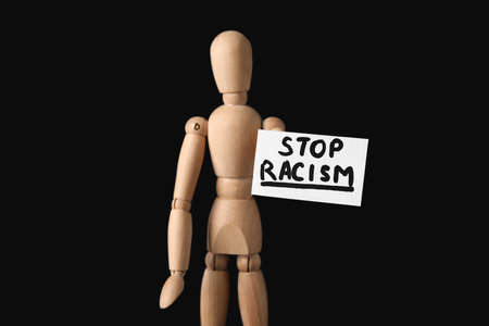 Wooden mannequin and paper sheet with text STOP RACISM on dark backgroundの写真素材