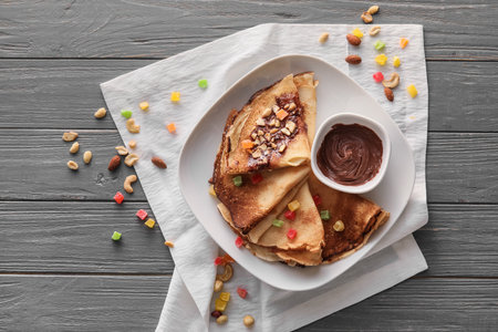 Plate of tasty thin pancakes with chocolate paste and nuts on gray wooden backgroundの写真素材