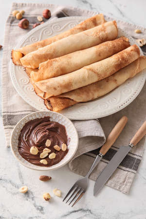 Plate of tasty thin pancakes with chocolate paste and nuts on white marble backgroundの写真素材
