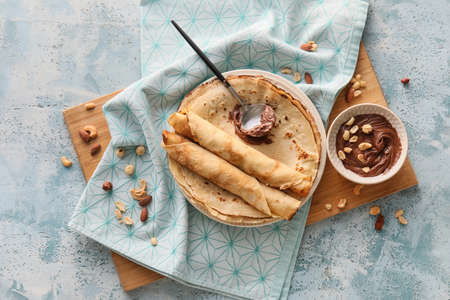 Plate of tasty thin pancakes with chocolate paste and nuts on blue backgroundの写真素材