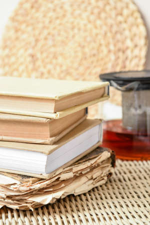 Stack of books with teapot on wicker tray, closeup