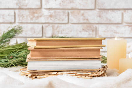 Stack of books with candles and fir branches on plaid near brick wallの写真素材