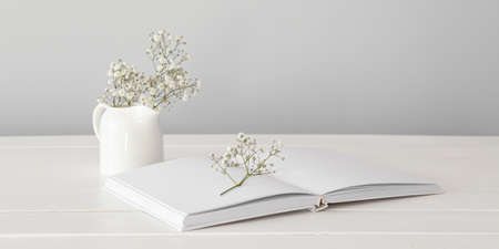 Open book with jug and flowers on white wooden table against light backgroundの写真素材