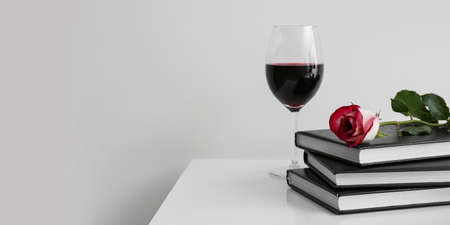 Books, rose flower and glass of wine on table against light background with space for textの写真素材