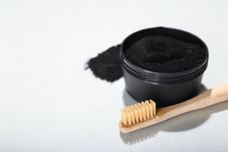 Jar with activated charcoal tooth powder and toothbrush on white background