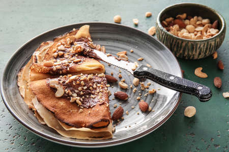Plate of tasty thin pancakes with chocolate paste and nuts on green backgroundの写真素材