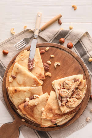 Board of tasty thin pancakes with chocolate paste, cut banana and nuts on white wooden backgroundの写真素材