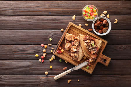 Board of tasty thin pancakes with chocolate paste and nuts on dark wooden backgroundの写真素材