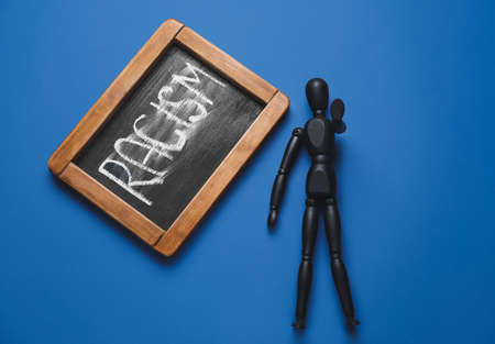 Chalkboard with written word RACISM and black mannequin on color backgroundの写真素材