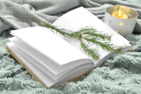 Opened book with blank pages, fir tree branch and burning candle on soft plaidの写真素材
