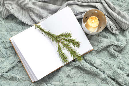 Burning candle, book with blank pages and fir tree branch on soft plaid