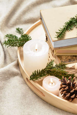 Wooden tray with burning candles, fir tree branches and books on plaidの写真素材