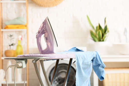 Board with electric iron and shirt in laundry room