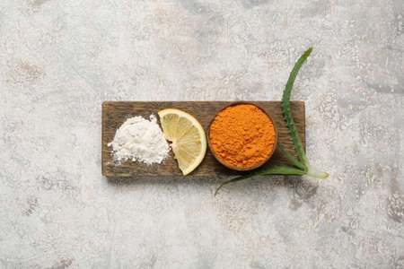 Board with turmeric powder and lemon on light background