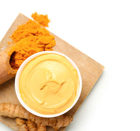 Bowl with turmeric mask and powder on white background