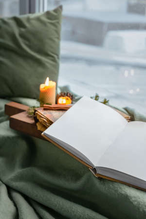Opened book with blank pages, burning candles and winter decor on windowsill