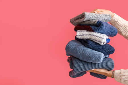 Woman with stack of warm knitted sweaters near pink wallの写真素材