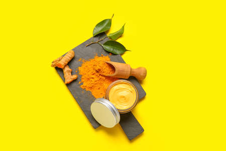 Board with jar and ingredients for turmeric mask on yellow backgroundの写真素材