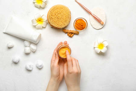 Female hands with jar of turmeric mask on light backgroundの写真素材