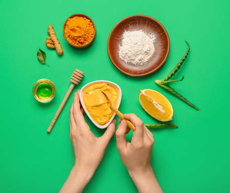 Woman stirring turmeric mask in bowl on green backgroundの写真素材