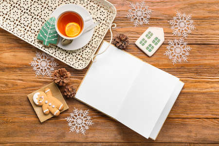 Opened book with blank pages, cup of tea, cookies and winter decor on wooden backgroundの写真素材