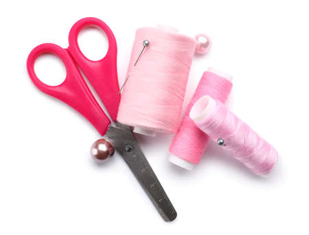 Pink sewing thread spools with pins and scissors on white background