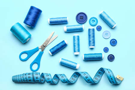Sewing thread spools, buttons, scissors and measuring tape on color backgroundの写真素材