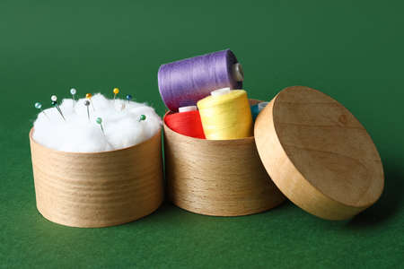 Wooden boxes with sewing thread spools and pins on color background