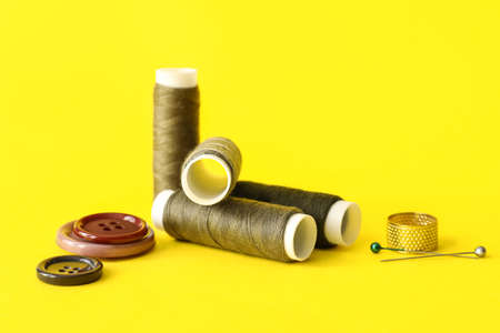 Sewing thread spools, pins, thimble and buttons on color background