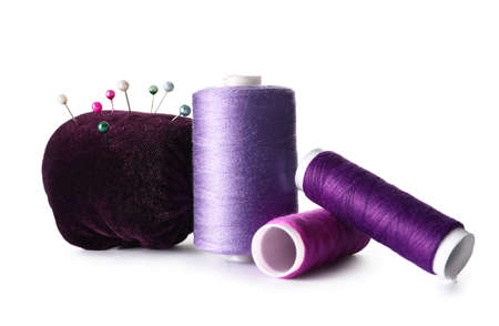 Purple sewing thread spools and pincushion with pins on white background