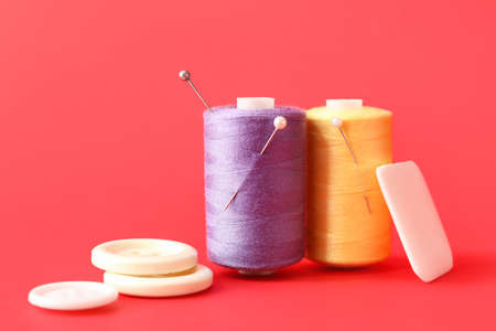 Sewing thread spools with pins, buttons and pieces of soap on color backgroundの写真素材
