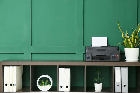 Shelf unit with modern printer, houseplant and folders near green wallの写真素材
