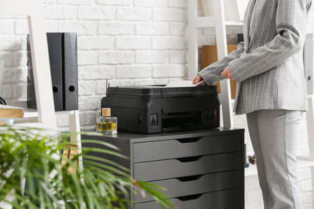 Businesswoman using printer on chest of drawers near white brick wall