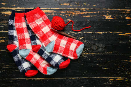 Warm socks, knitting yarn and crochet hook on dark wooden background