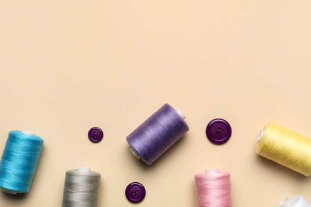 Sewing threads with buttons on beige background