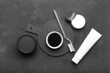 Bowl with activated charcoal tooth powder, tube and toothbrush on dark background
