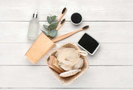 Bowls with activated charcoal tooth powder, brushes and bath accessories on white wooden background