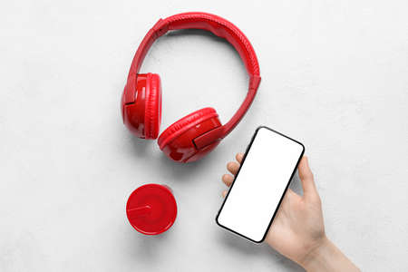 Female hand with mobile phone, headphones and wireless portable speaker on light backgroundの写真素材