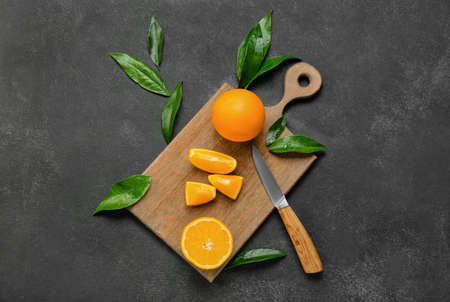 Wooden board with cut juicy oranges on black background