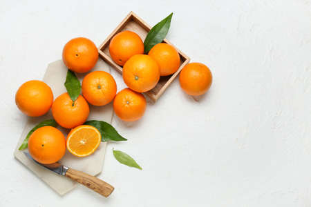 Wooden box and board with fresh juicy oranges on white background