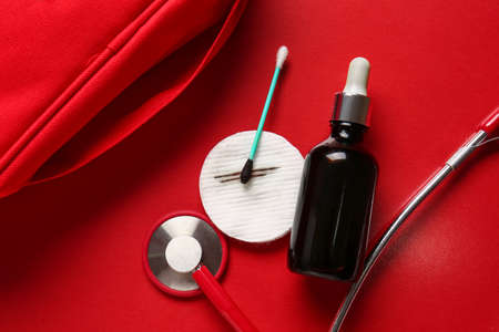 Bottle with iodine, cotton pad, swab and stethoscope on red background