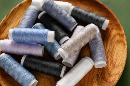 Heap of coils with different sewing threads on wooden plate