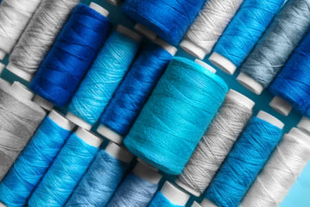 Closeup view of spools with gray and blue sewing threads as background