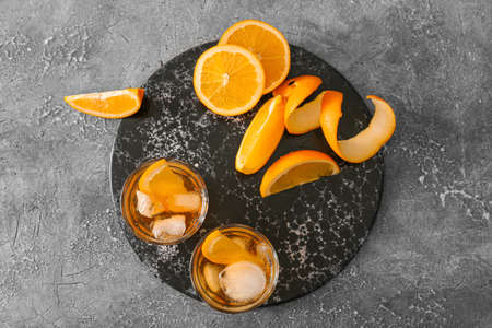 Glasses of tasty Old Fashioned Cocktail and orange on gray background