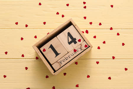 Calendar with date of Valentines Day and heart shaped confetti on yellow wooden backgroundの写真素材